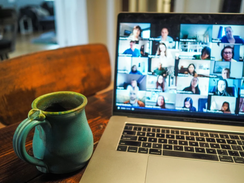 A laptop displaying a training video call with multiple participants, next to a turquoise ceramic mug on a wooden table.